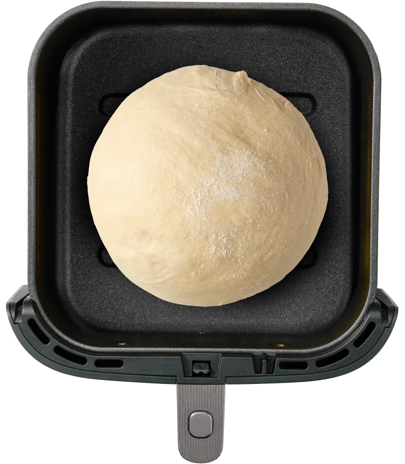 A round ball of dough sits in a square, non-stick cooking tray. The surface is lightly dusted with flour.