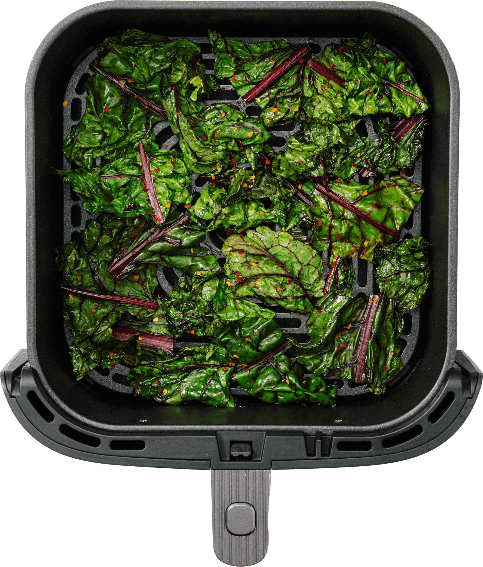 A black air fryer basket filled with vibrant green kale leaves, sprinkled with red seasoning.